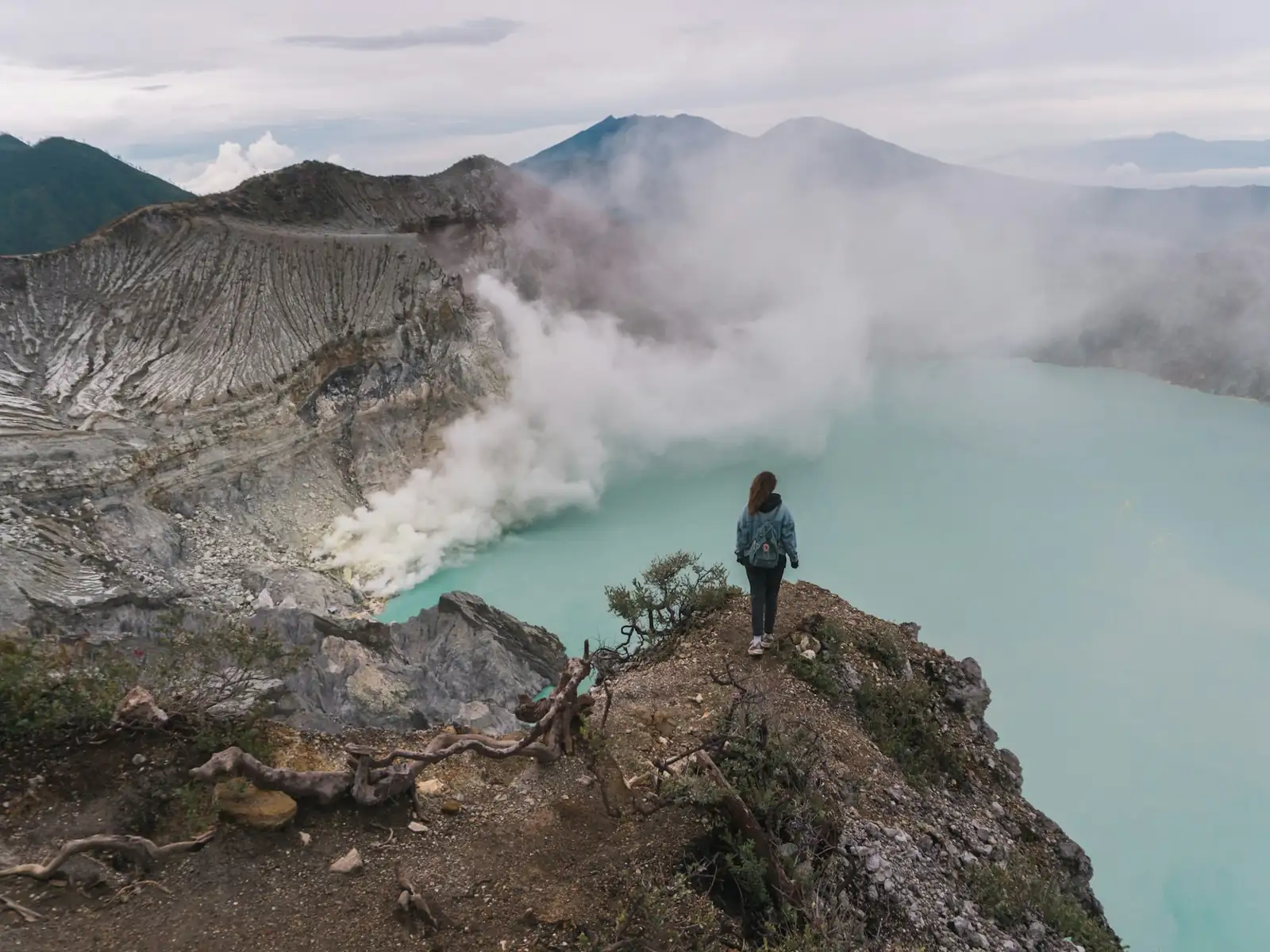 Traveller standing on the Kawah Ijen crater rim above the steaming turquoise lake