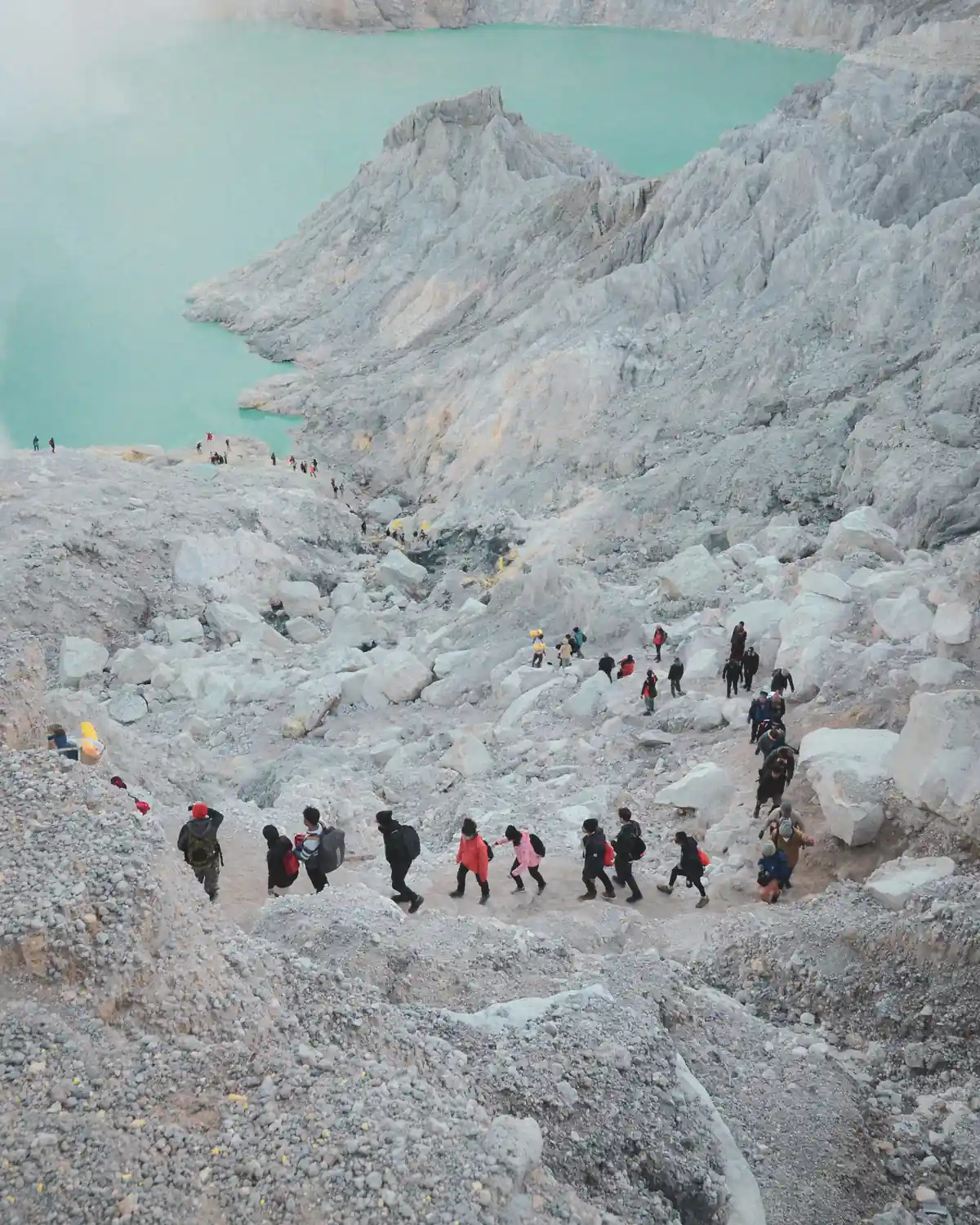 Trekkers walking the rocky trail on the Kawah Ijen crater rim beside the turquoise lake