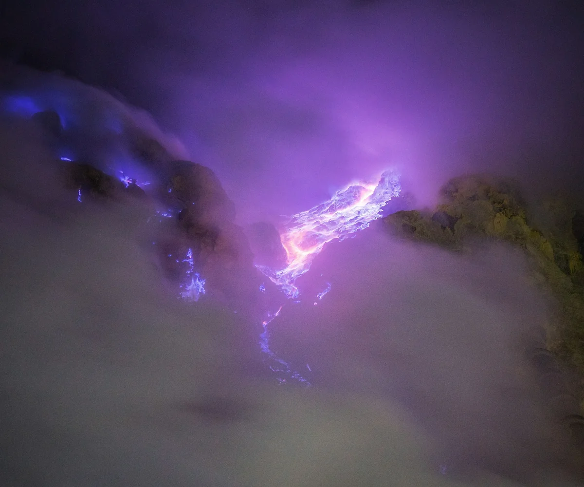 Blue sulfur flames burning among rocks inside the crater